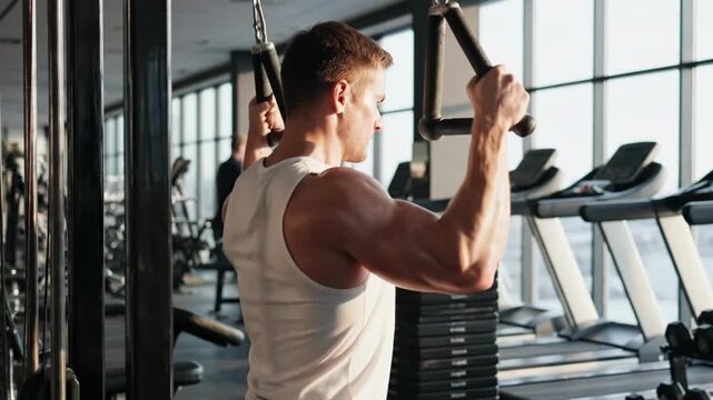 Muscular man performing triceps pushdown exercise in a bright gym
