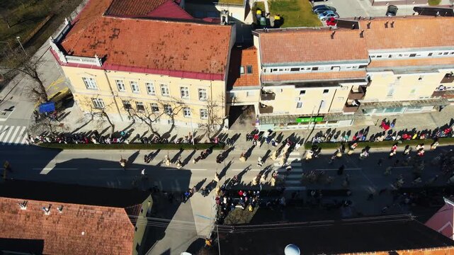 Drone aerial view of Pust carnival parade with crowd and traditional festival in Ormoz Slovenia