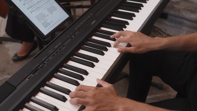 Hands playing piano keyboard with tablet displaying sheet music