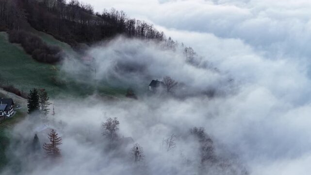 Hillside houses and trees covered by fog near Walensee Switzerland