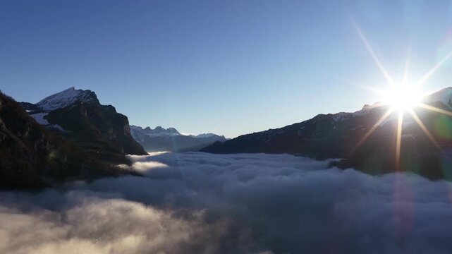 Breathtaking aerial view of a thick sea of fog covering Lake Walensee. Jagged Alpine peaks pierce the white cloud layer under a clear, sunlit winter sky in Switzerland.