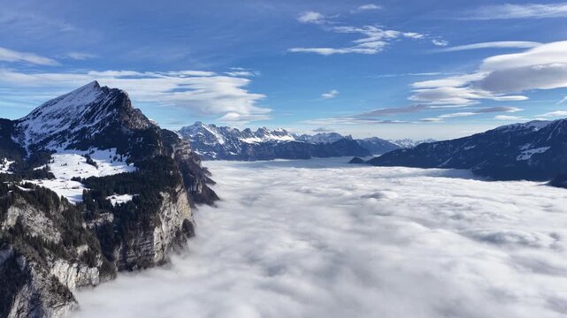 Walensee Swiss alps near Amden and Walenstadt, Switzerland above cloud inversion, snowy alpine mountains rising over fog filled valley under blue sky.