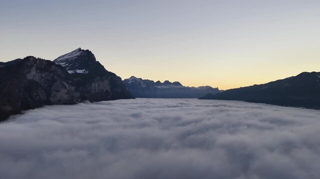 Dramatic aerial view of Swiss peaks floating over a dense sea of fog. The hidden Walensee valley creates a mystical, high-altitude winter landscape near Walenstadt.