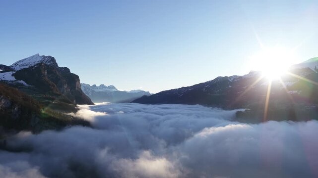 Aerial view of the jagged Churfirsten peaks rising from a thick sea of fog. A minimalist winter landscape showing the dramatic isolation of the Swiss Alps.