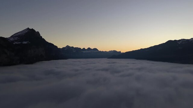 Walensee region Switzerland drone flight above sea of clouds at sunrise near Walenstadt and Amden, Swiss alps mountains rising from fog with calm dawn sky and alpine landscape.