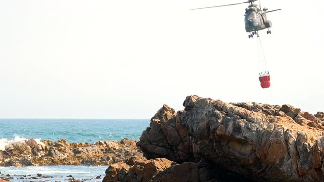 Firefighting helicopter ascends after scooping seawater with bambi bucket, slomo