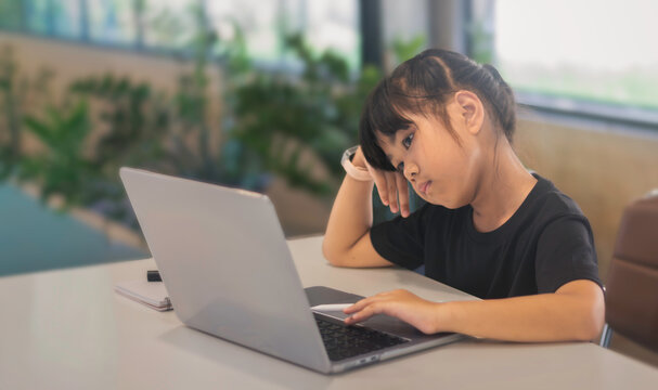 Tired child using laptop for online learning, fatigue and screen time concept at home or cafe.
