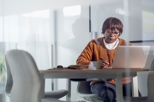 Senior female entrepreneur working in meeting room seen through glass