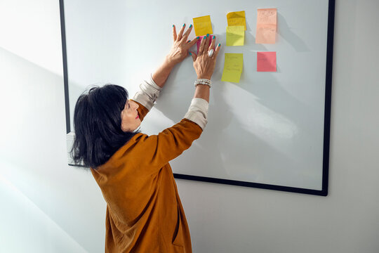 Senior businesswoman sticking adhesive note on whiteboard in meeting room