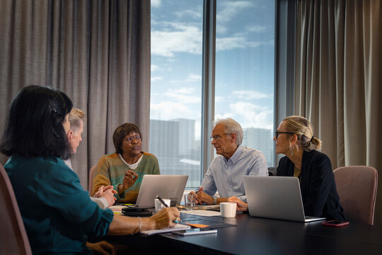 Mature female business professional explaining strategy to colleagues while sitting in office board room