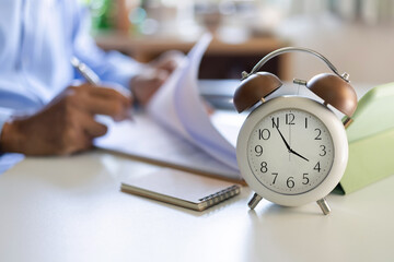 close up at alarm clock 4PM. blurred background asian businessman working in evening with documents...