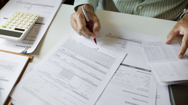 close up shot, man hand holding pen checking business contract, passbook and other documents before sign to apply for a business startup loan, doing online business E-commerce