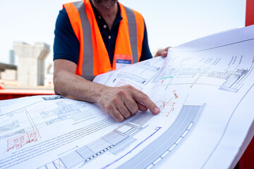 Engineer reviewing architectural blueprints outdoors.