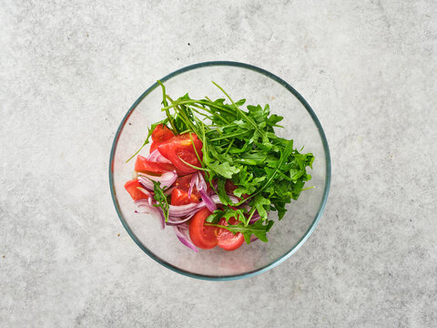 Fresh salad ingredients are mixed together in a glass bowl for a healthy meal preparation