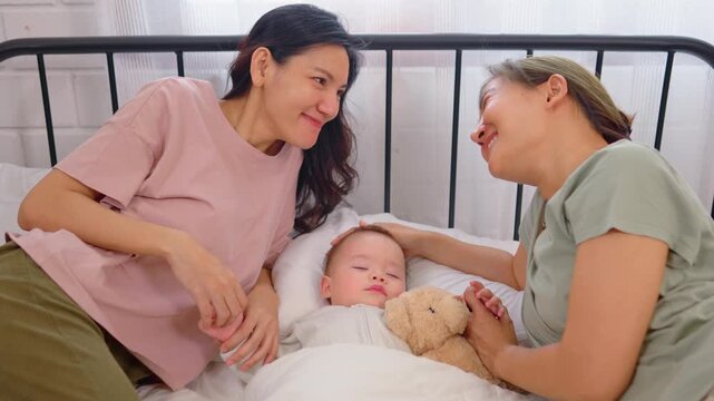 Asian lesbian couple lovingly caring for and raising their baby boy at home. 