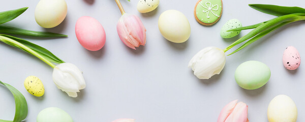 Naklejka premium Happy Easter composition. Easter eggs on colored table with yellow Tulips. Natural dyed colorful eggs background top view with copy space