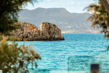 Rocky coastal island surrounded by turquoise sea water with distant mountains in background. Scenic...