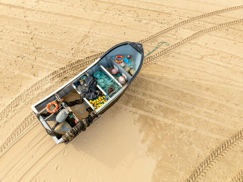 Aerial view of a fishing boat stranded on the sandy beach, its hull filled with nets, floats, and gear casting shadows on the warm sand, Goa, India.