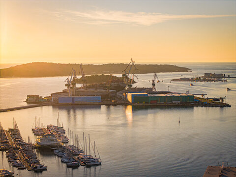 Aerial view of the shipyard basks in the golden light of dawn, contrasting with the calm, deep blue waters surrounding it, Pula, Istria County, Croatia.