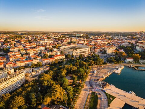 Aerial view of the iconic Pula Arena standing proudly amidst the urban tapestry, where terracotta rooftops meet the azure Adriatic, Pula, Istria County, Croatia.