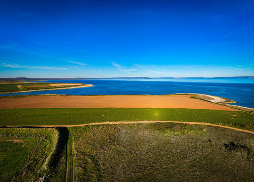 Aerial view of the contrasting green fields and golden farmlands meeting the deep blue Adriatic sea under a clear sky., Liznjan, Istria County, Croatia.