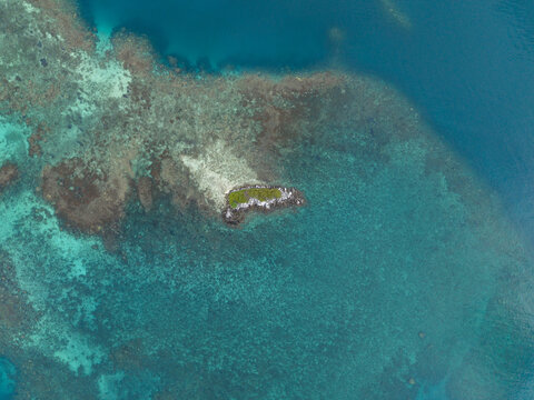 Aerial view of a small island surrounded by coral reefs in the turquoise waters of the ocean at Camar Rock Island, Jepara Regency, Central Java, Indonesia.