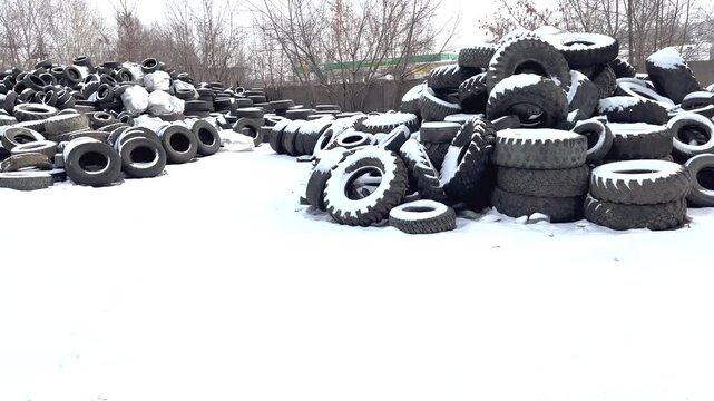 Old tires are piled up in a recycling yard. The cold weather is clear in the snowy setting. The focus is on reusing rubber and managing waste. Efforts towards ecology and resource recovery are shown.