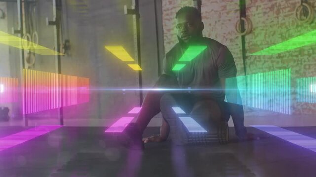 Vertical video: Resting after set man in shorts shifting torso on gym floor with rings, light bars