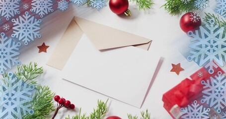 Displaying blank white greeting card resting atop open kraft envelope on tabletop, with red bauble © vectorfusionart