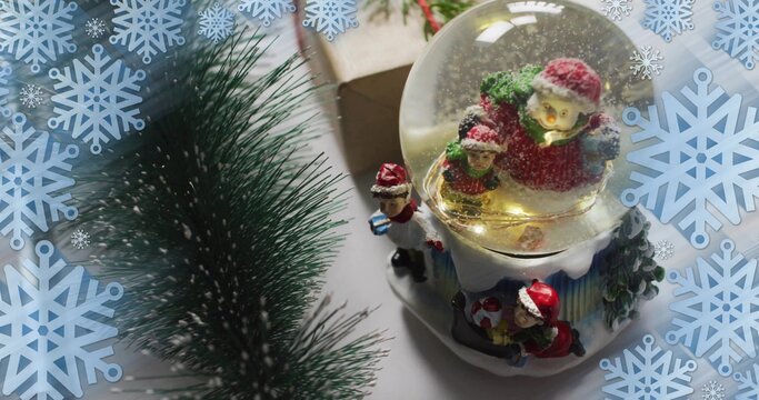 Showing lit snow globe on holiday tabletop with glittering Santa base and pine, copy space