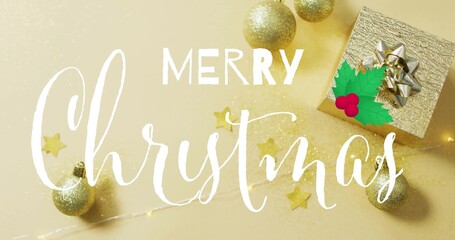 Showing white handwritten Merry Christmas script on gold backdrop with gift box, silver bow, holly