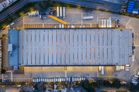 Aerial view of a vast distribution center with orderly rows of trucks and trailers under the soft glow of evening lights, Settecamini, Lazio, Italy.