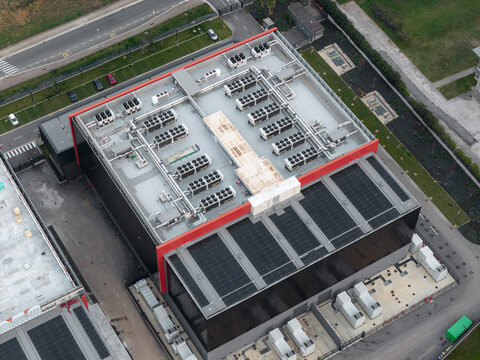 Aerial view of a modern data center with a red trim and complex rooftop machinery, juxtaposed against green spaces, Settecamini, Lazio, Italy.