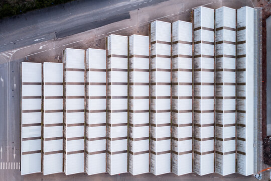 Aerial view of a geometric pattern of white roofs contrasting with the dark asphalt, casting sharp shadows in the March sunlight, Settecamini, Lazio, Italy.