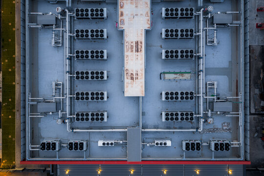 Aerial view of a data center rooftop covered in intricate networks of pipes and machinery under a soft light, Settecamini, Lazio, Italy.