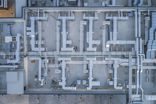 Aerial view of a network of ducts and pipes creating an intricate geometric pattern on a rooftop, a stark contrast of industrial precision against the urban landscape, Settecamini, Lazio, Italy.