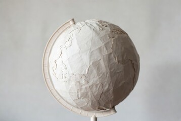 Paper mache globe on plastic stand, light cream tones, hand-crafted Earth model on white background.