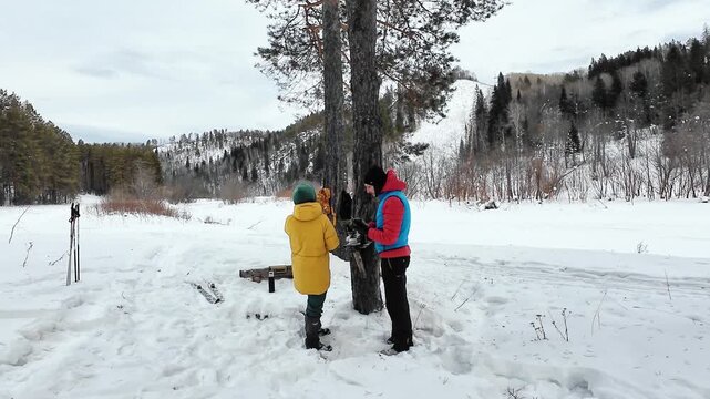 Couple Sharing Warmth Outside. Enjoying Hot Drinks In Snowy Forest. Man And Woman Smile Amid Frosty Pine Trees. Winter Scenery Setting With Couple Exchanging Warmth And Cheerful Expressions