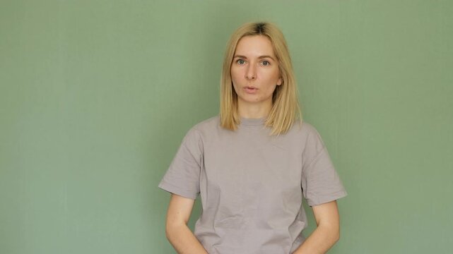 Middle-aged blonde woman speaking and gesturing while looking directly at the camera. Professional speaker presenting information or giving a speech against a solid green background