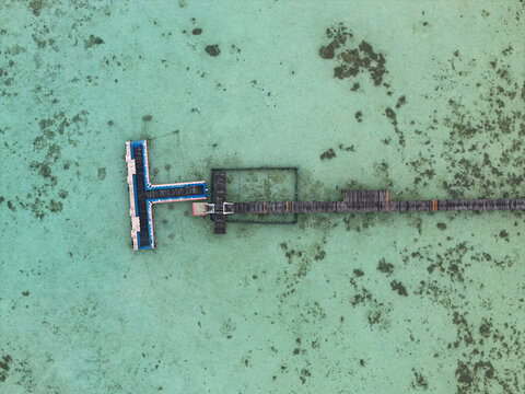 Aerial view of a pier stretching into the turquoise sea, contrasting against the dark wooden structure at Turtle Conservation, Karimunjawa, Central Java, Indonesia.