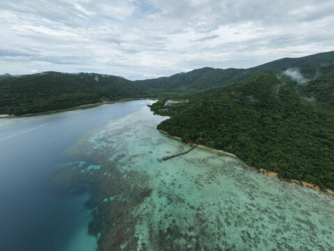 Aerial view of the shimmering turquoise water meeting the vibrant green shoreline, fringed by a wooden pier, Turtle Conservation, Karimunjawa, Central Java, Indonesia.