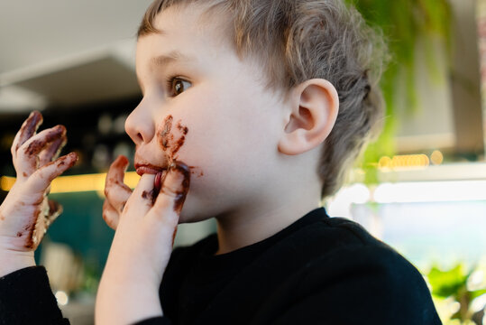 Side profile of a three year old boy licking melted chocolate from fingers. Focus on action and messy hand. Concept of unhealthy eating habits and allergy risk in childhood.
