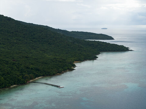 Aerial view of verdant island slopes meet the tranquil turquoise sea, a pier stretching into the calm waters at Turtle Conservation, Karimunjawa, Central Java, Indonesia.