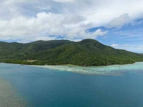 Aerial view of lush green island meets the turquoise sea under a sky dappled with soft white clouds, Turtle Conservation, Karimunjawa, Central Java, Indonesia.