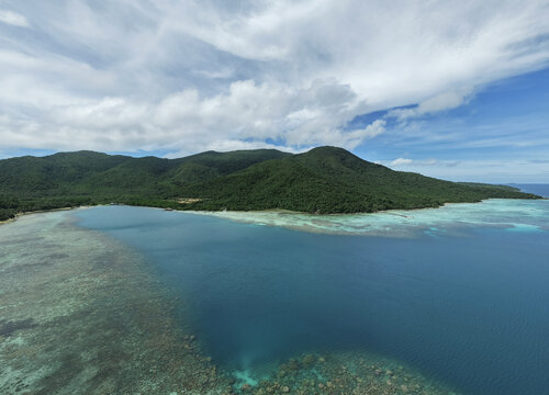 Aerial view of the lush green island meeting the clear turquoise waters under a bright sky, Turtle Conservation, Karimunjawa, Central Java, Indonesia.