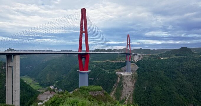 Bridge spanning across deep green valley with massive red towers and cable-stayed design in Guizhou, China.