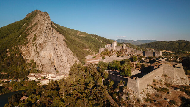Aerial view of the imposing Citadelle de Sisteron stands guard against the towering Rocher de la Baume, a fortress of stone against nature's raw majesty, Sisteron, Provence-Alpes-Cote d'Azur, France.