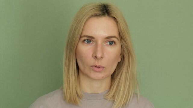 Attractive middle-aged woman performing facial exercises against aging, showing techniques for lifting the oval of the face and getting rid of wrinkles with cheek-puffing movements
