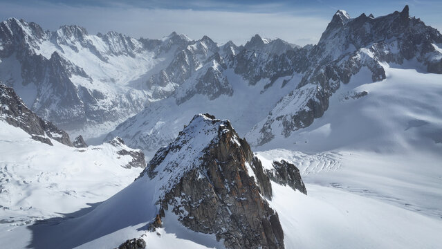 Aerial view of a stark, snow-clad mountain range, where jagged peaks pierce the sky above a pristine, white expanse, Vallee Blanche, Chamonix, Auvergne-Rhone-Alpes, France.