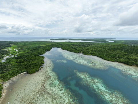 Aerial view of the vivid turquoise waters meeting the emerald green mangrove forests under a cloudy sky, Karimunjawa, Central Java, Indonesia.